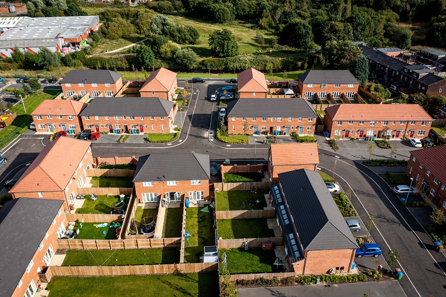 aerial footage of a residential road with houses, gardens and driveways