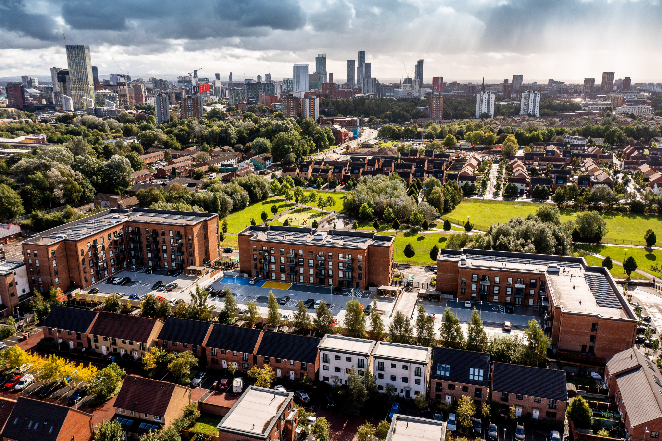 aerial shot of three apartment buildings overlooking a green park with Manchester city centre in the distance