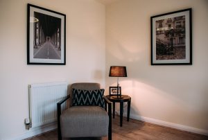 Armchair, table and lamp in corner of room with pictures on the walls