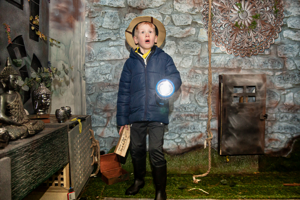 small boy in explorer hat has a shocked expression whilst holding a torch