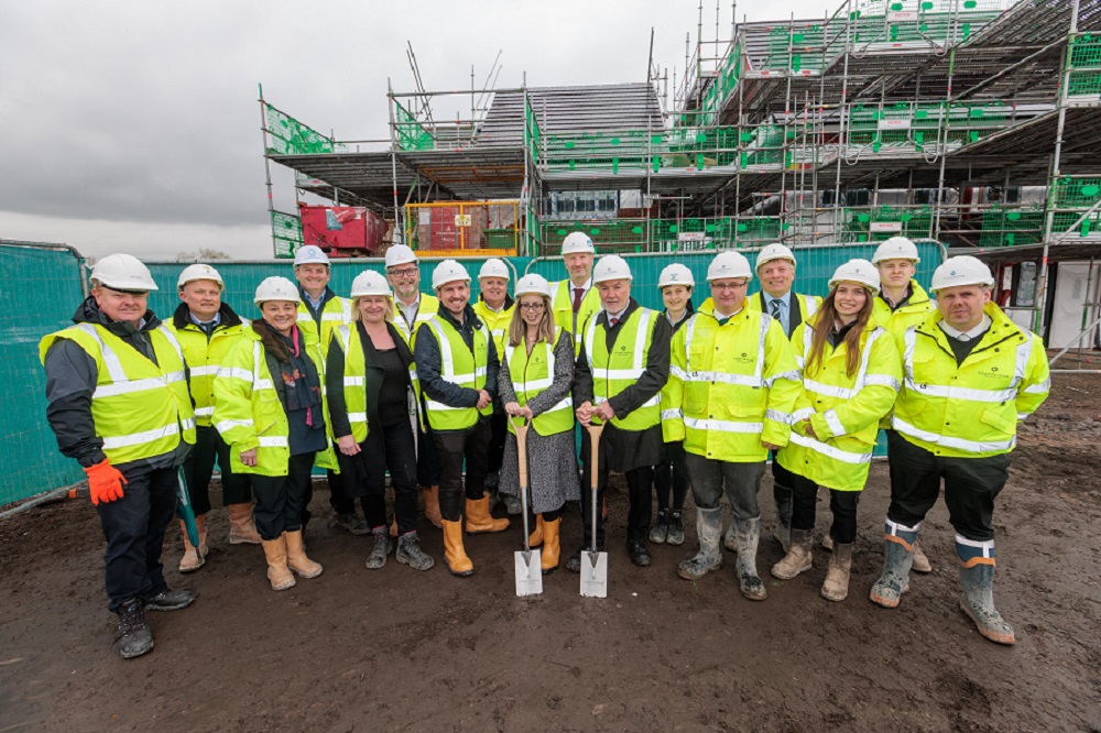 A group of people in hi-vis jackets pose on a construction site