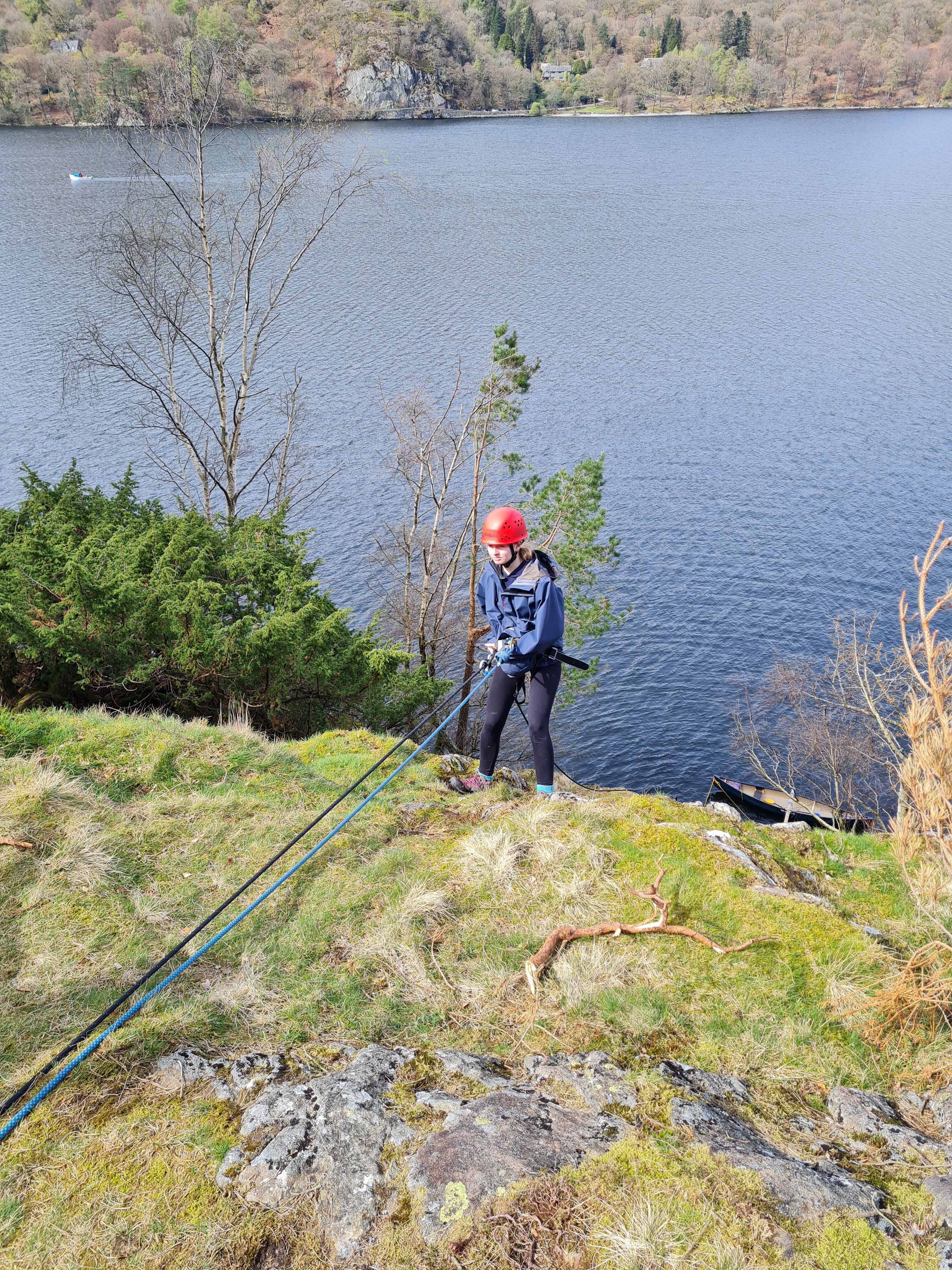 A girl in a red helmet abseils over a lake