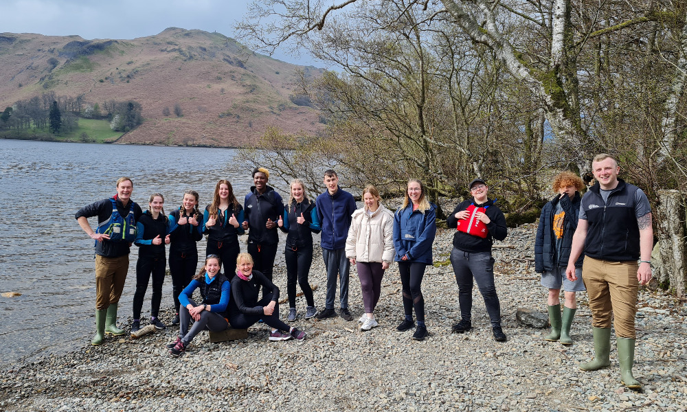 A group of people stand on the edge of a lake smiling