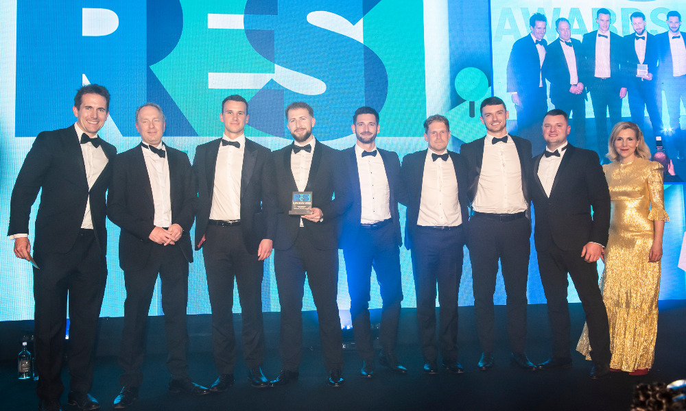 8 men in suits accept an award from a woman in a gold dress