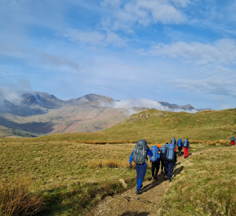 a group of people in blue rucksacks hike along a mountain trail