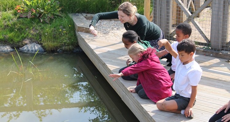 Children kneel down next to a pond