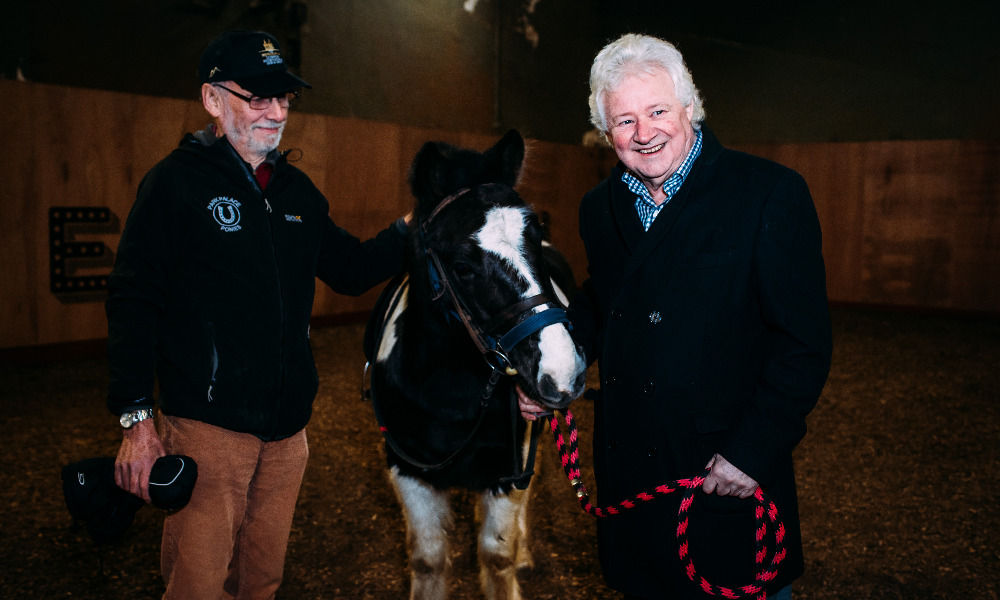 Two men stand either side of a small black and white pony