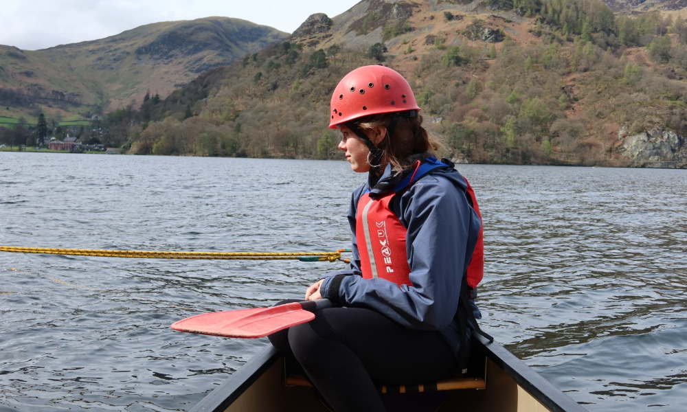 A young woman in a red helmet sits on the edge of a boat on a lake
