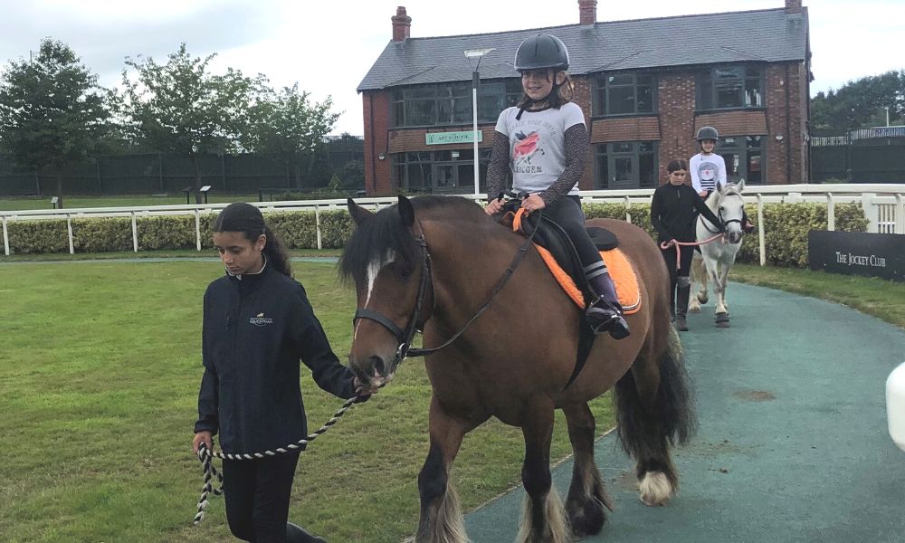 A young girl sits on a brown horse being led by a young girl