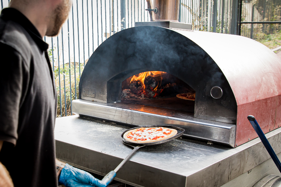 Pizza being taken out of a woodfired oven