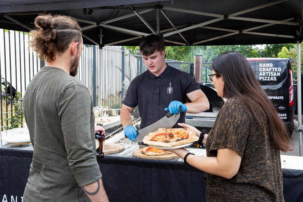 A man serves pizza to two people